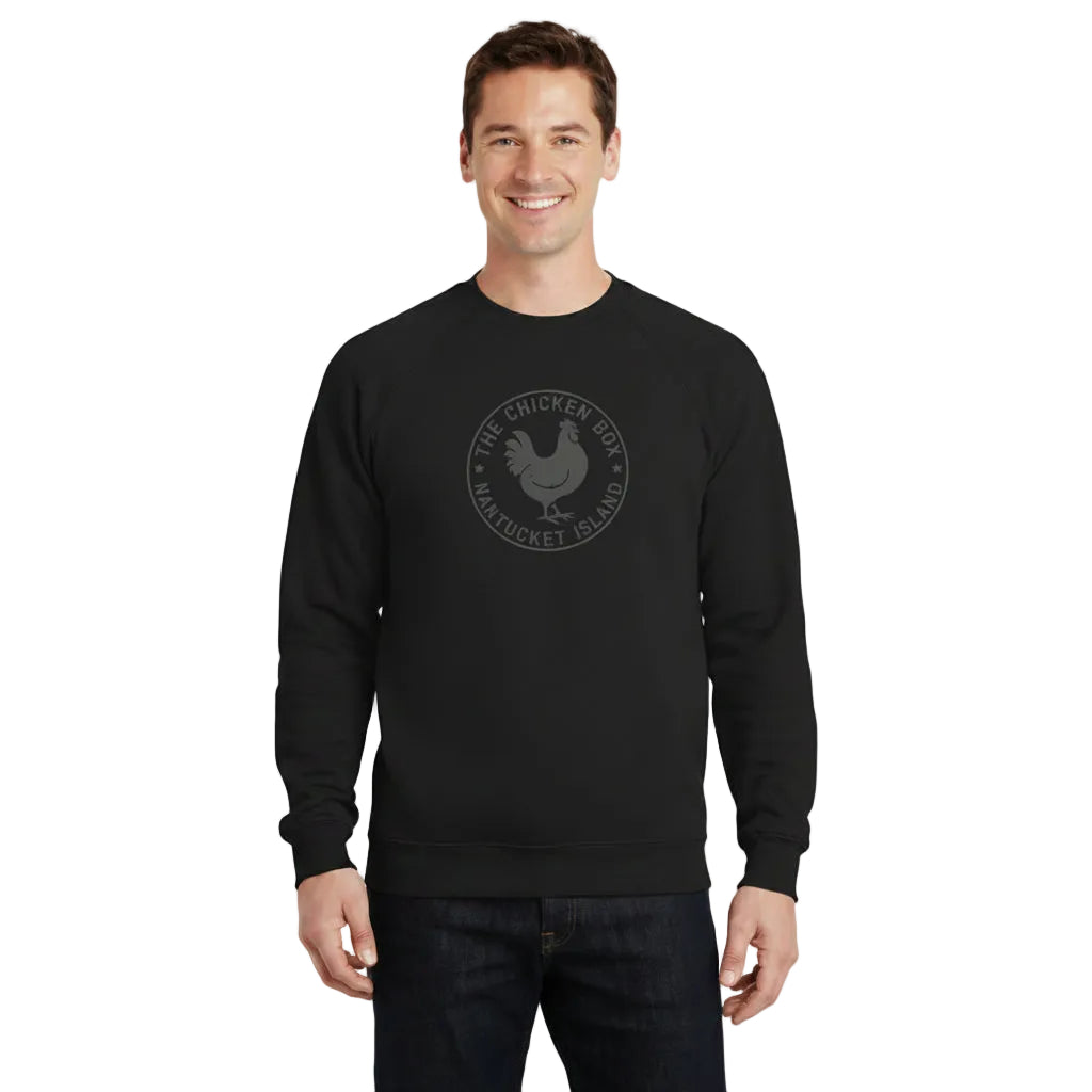 A man wearing a black crewneck sweatshirt with a circular white graphic on the chest, paired with dark jeans, against a plain white background.